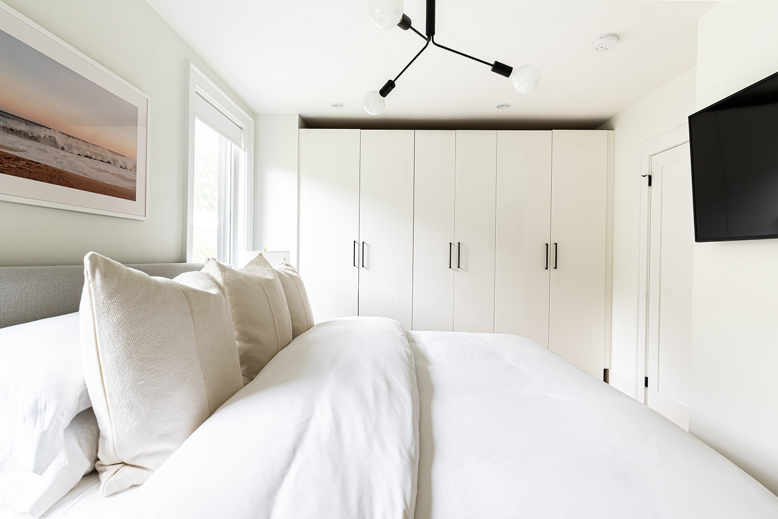 A white bedroom with a tv above the bed.