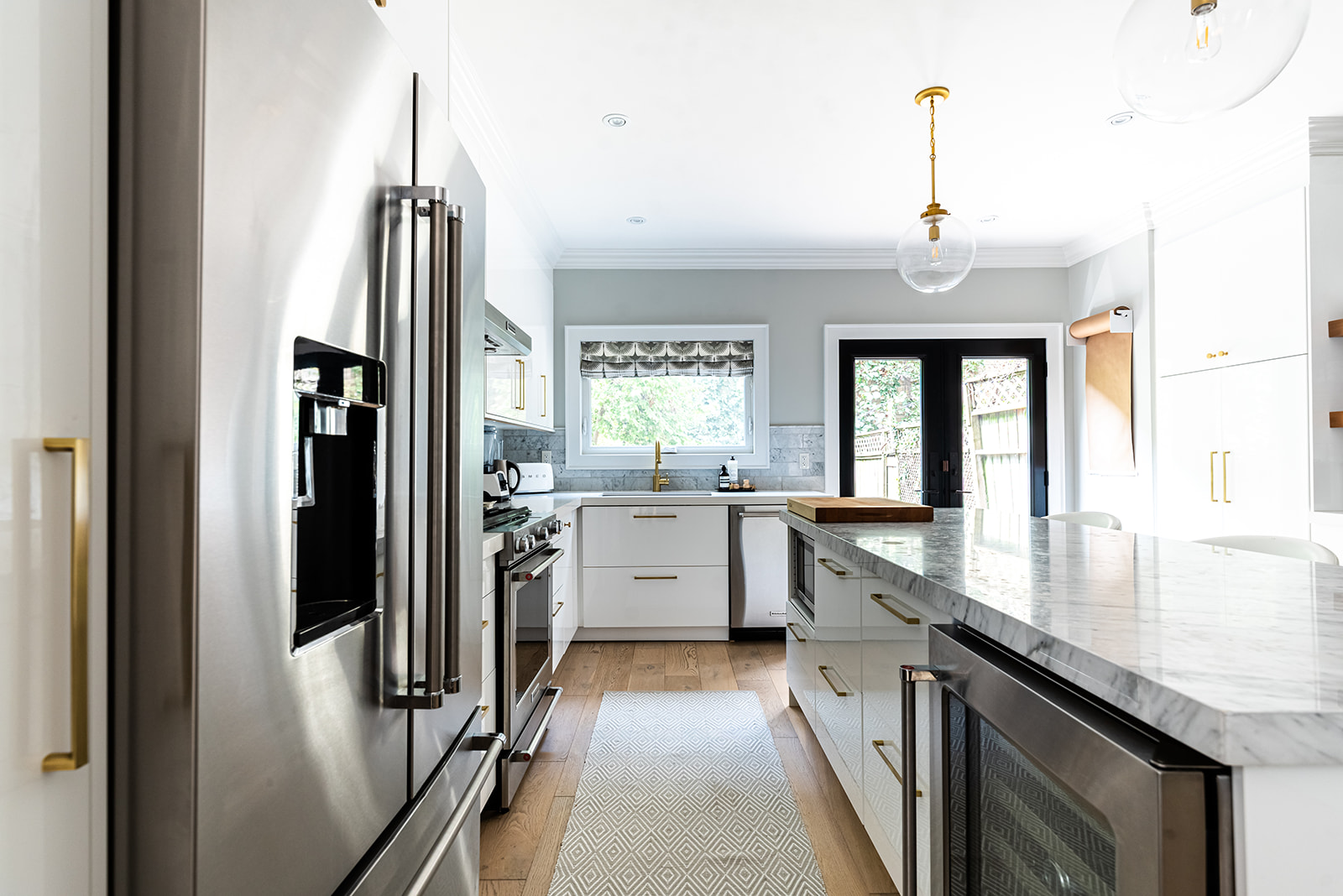 A white kitchen with a marble counter top and stainless steel appliances.