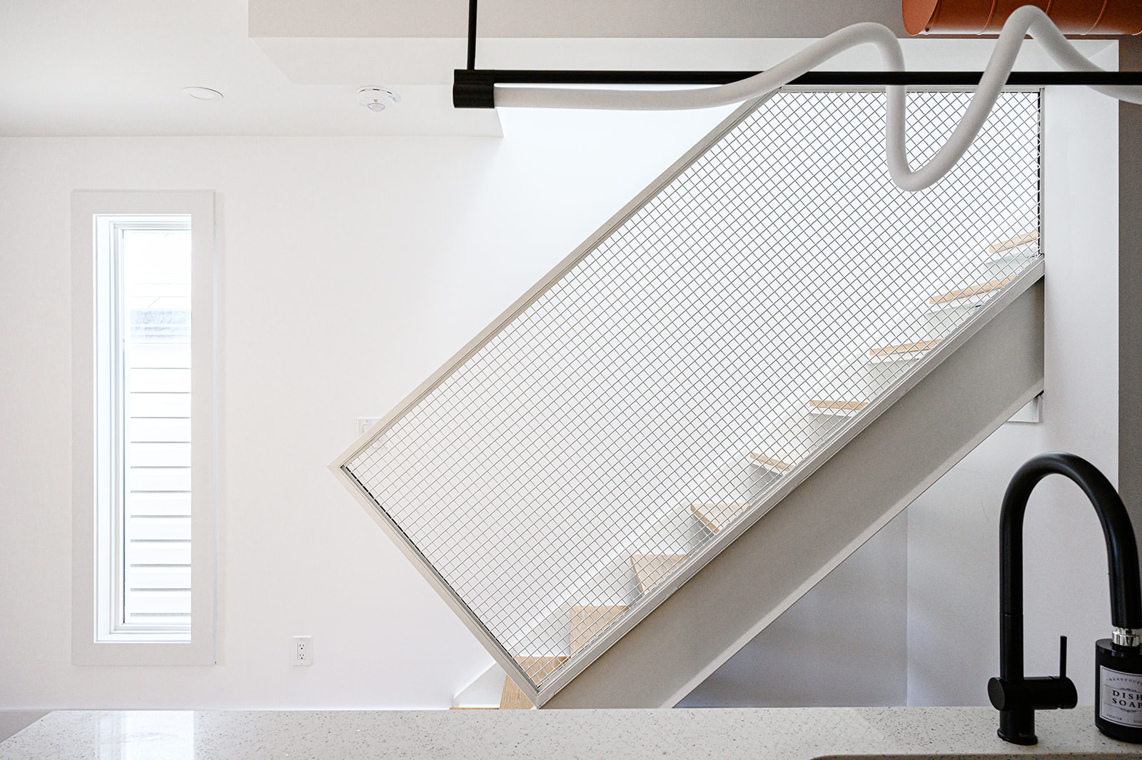 A white kitchen with a sink and a stairway.